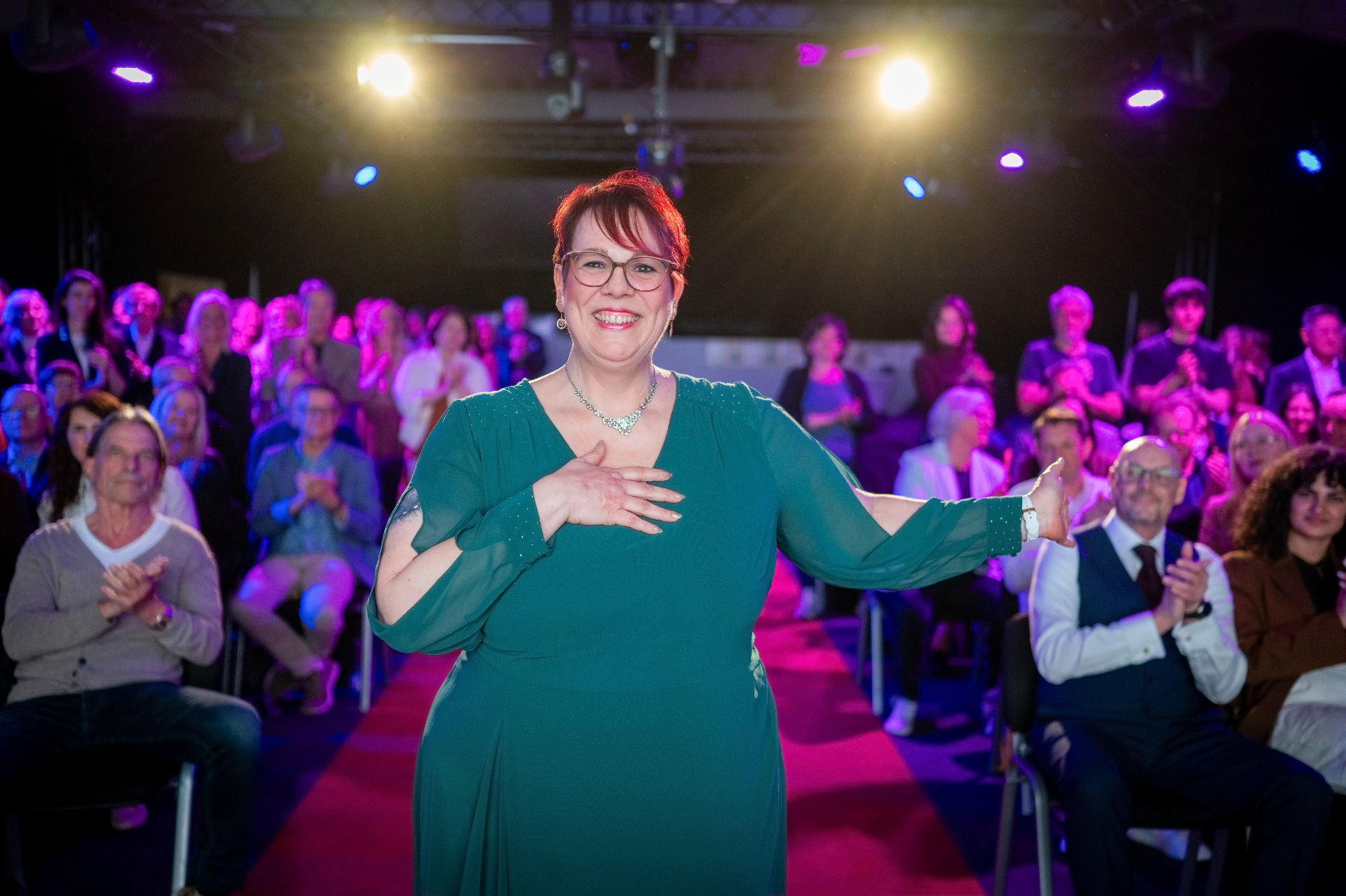 Nicole Frontzek auf der Bühne beim Internationalen Speaker Slam, applaudierendes Publikum im Hintergrund